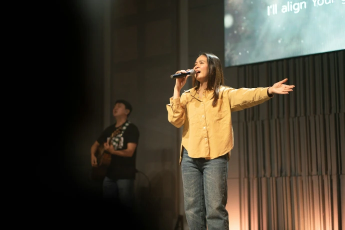 Woman singing on stage with man playing guitar.